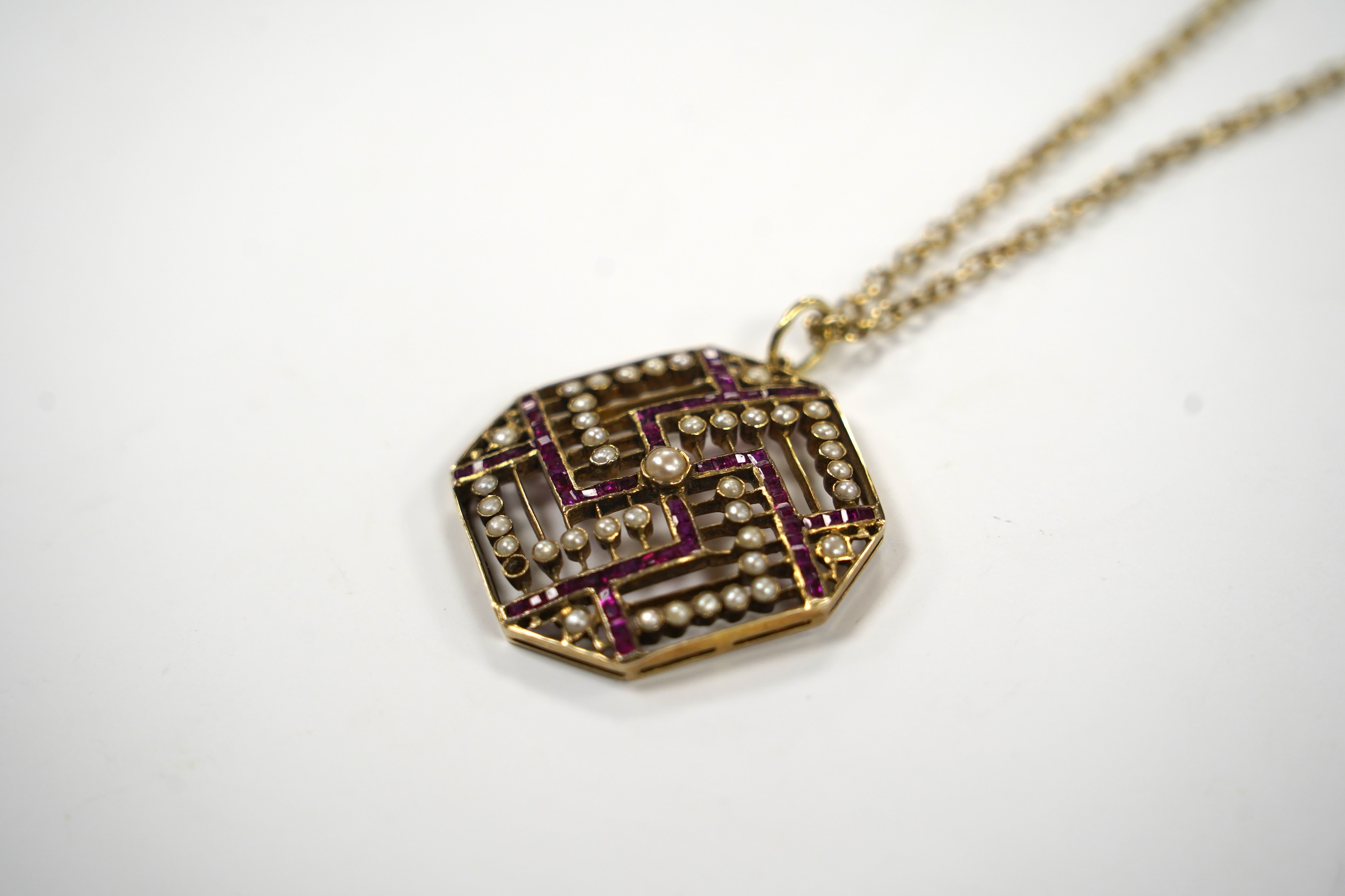 An Edwardian 15ct, ruby and seed pearl set octagonal pendant, 35mm, gross weight 9.7 grams, on a gilt metal chain.